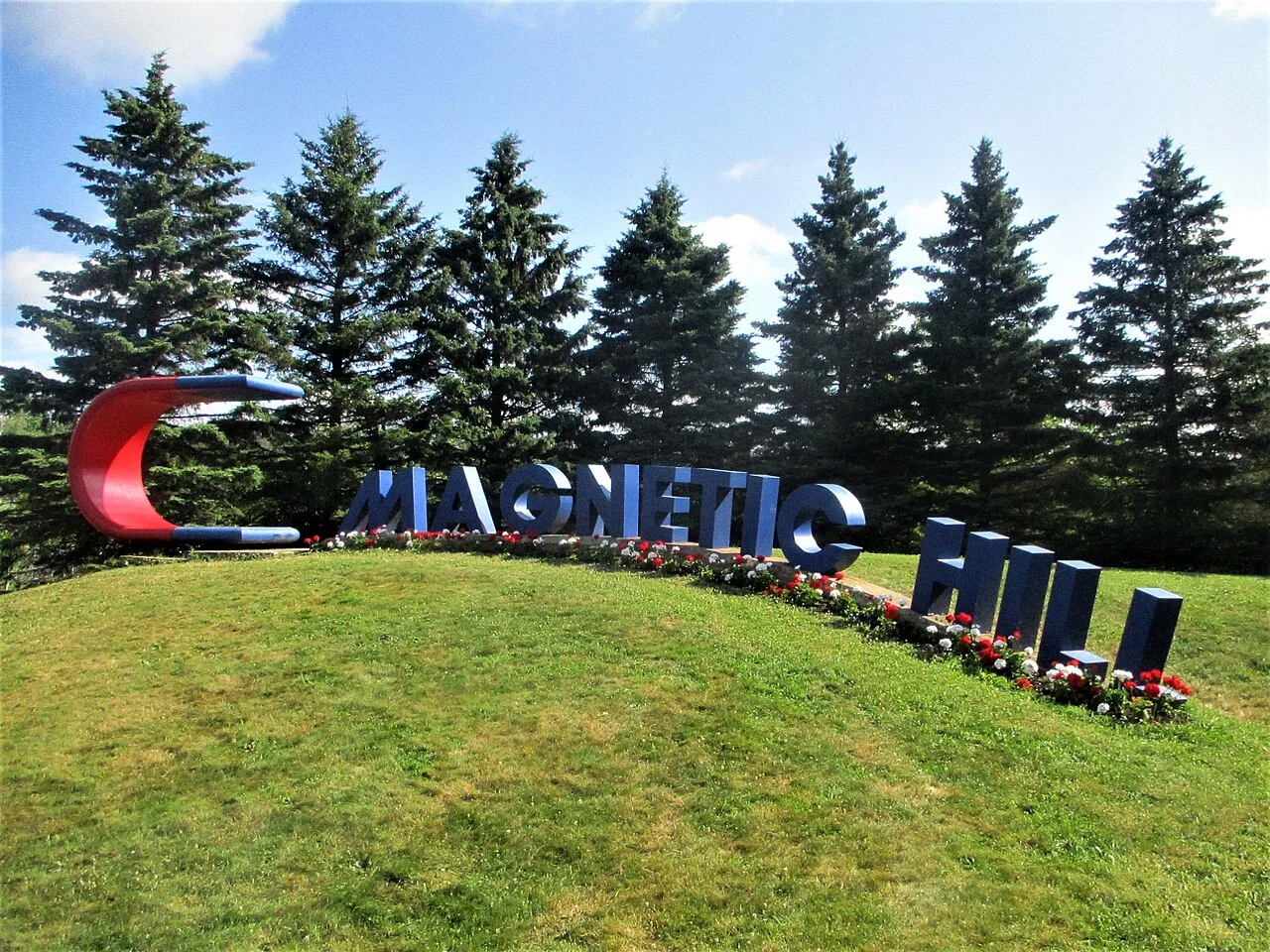 Photograph of the Magnetic Hill site sign in Moncton, New Brunswick, giant blue letters and a red horseshoe magnet sculpture on a grassy hill