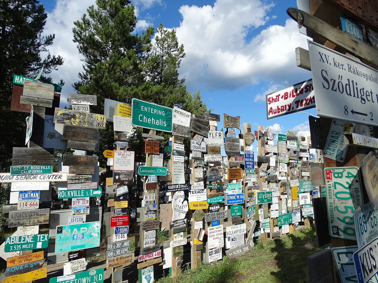 Photograph of the Sign Post Forest in Watson Lake, Yukon, hundreds of town signs and licence plates nailed to wooden posts under a blue sky