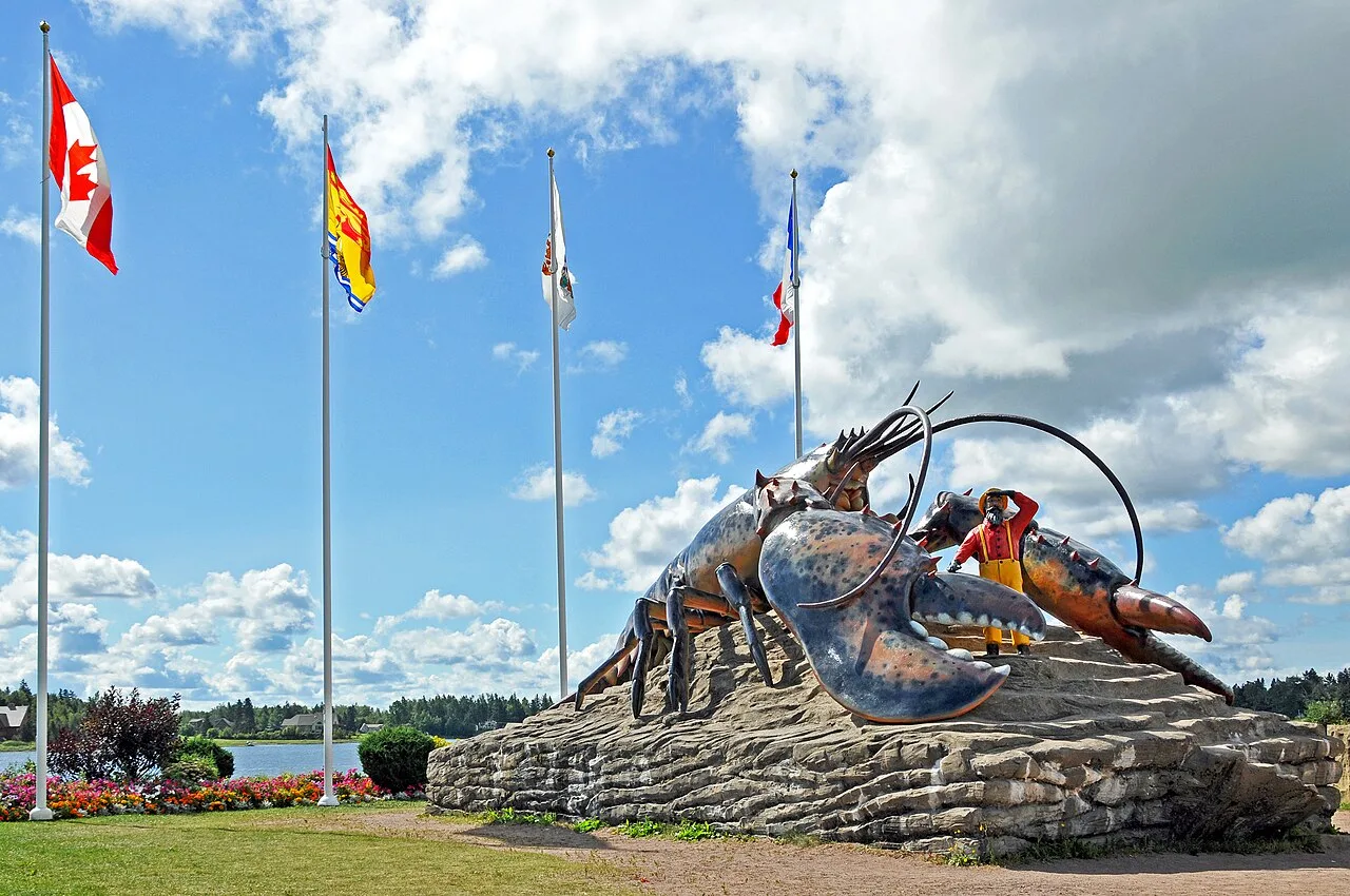 Photograph of the World's Largest Lobster sculpture in Shediac, New Brunswick, a giant lobster with a fisherman figure on a rock base beside flagpoles